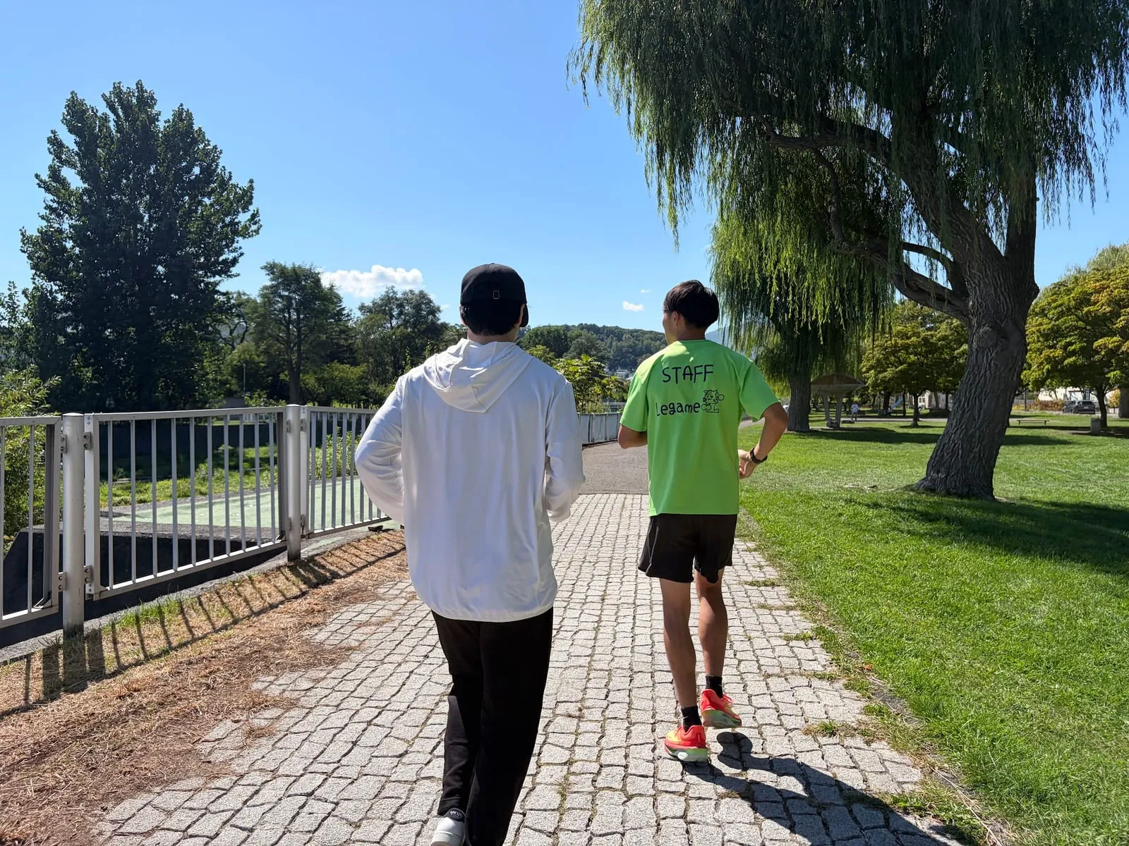 柵のある遊歩道を並んで走る2人(後ろ姿)